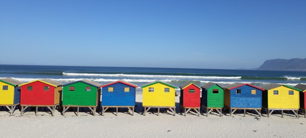 red, blue, yellow and green huts on a beach in muizenberg in cape town